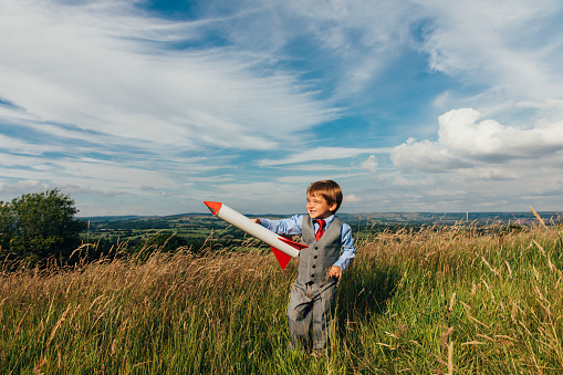 A young British boy dressed up in a business suit holds two rockets in his hands while standing on a grassy hill in the Peak District in the United Kingdom. On this sunny day, the boy dreams of becoming a successful businessman. Image taken in Leek, United Kingdom.