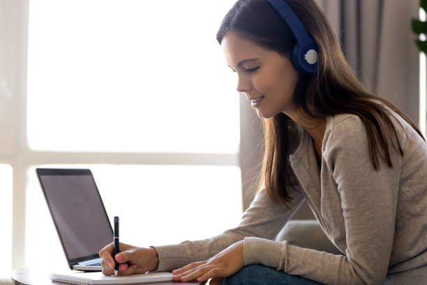 istock Focused woman in headphones writing notes, using laptop at home 1137821432