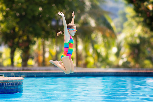 Child jumping and diving in swimming pool. Kids swim, jump and dive. Colorful rainbow swim wear for young kids. Little girl having fun on family summer vacation in tropical resort. Beach and water fun