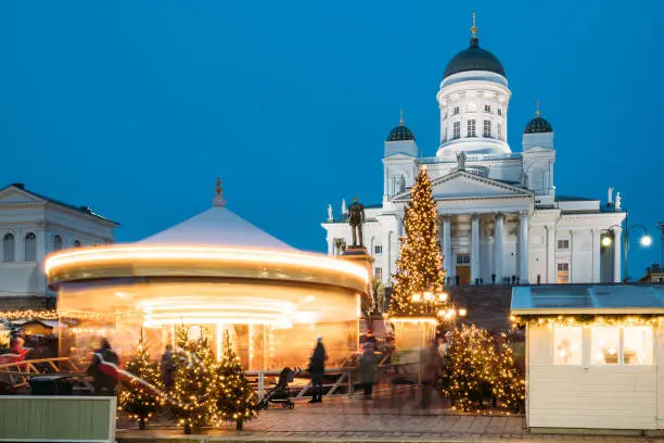 Photo of Helsinki, Finland. Xmas Market On Senate Square With Holiday Carousel And Famous Landmark Is Lutheran Cathedral And Monument To Russian Emperor Alexander II At Winter Evening