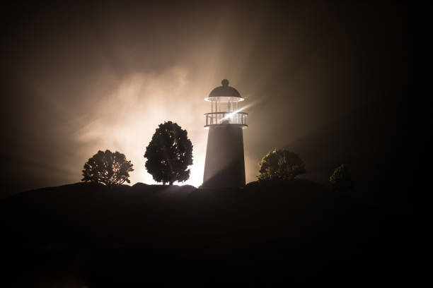 istock Lighthouse with light beam at night with fog. Old lighthouse standing on mountain. Table decoration. Toned background. Moonlighting. 1137826462