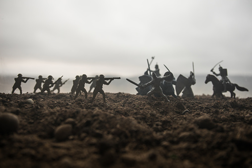 Battle scene. Military silhouettes fighting scene on war fog sky background. Creative concept. 20th century soldiers against medieval warriors. Artwork Decoration. Selective focus