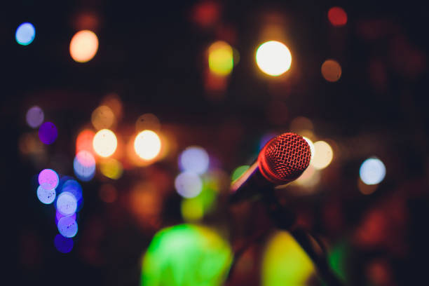 istock Microphone on a stand ready for live music performance or karaoke night with soft bokeh lights and people silhouettes in the background. Concept for musical singing event, having a good time. 1137845543