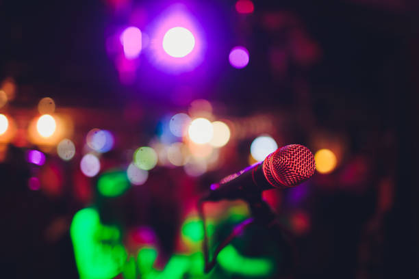 istock Microphone on a stand ready for live music performance or karaoke night with soft bokeh lights and people silhouettes in the background. Concept for musical singing event, having a good time. 1137845544