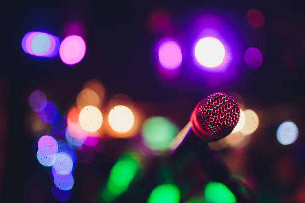 istock Microphone on a stand ready for live music performance or karaoke night with soft bokeh lights and people silhouettes in the background. Concept for musical singing event, having a good time. 1137845547