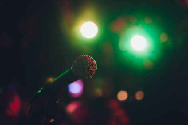 istock Microphone on a stand ready for live music performance or karaoke night with soft bokeh lights and people silhouettes in the background. Concept for musical singing event, having a good time. 1137845551