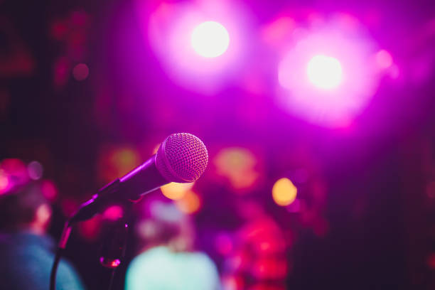 istock Microphone on a stand ready for live music performance or karaoke night with soft bokeh lights and people silhouettes in the background. Concept for musical singing event, having a good time. 1137845552