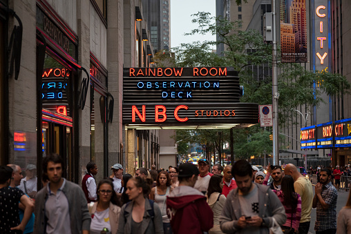 New York City, USA - July 9, 2016: A crowd of pedestrians walk past the iconic neon lights of NBC studios in Manhattan