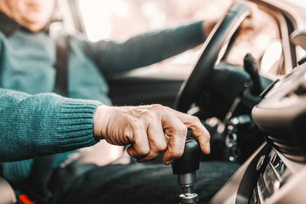 cerca de un hombre mayor sosteniendo una mano en el cambio de marchas y otro en el volante mientras está sentado en su coche. enfoque selectivo en la mano. - gearshift change gear car fotografías e imágenes de stock