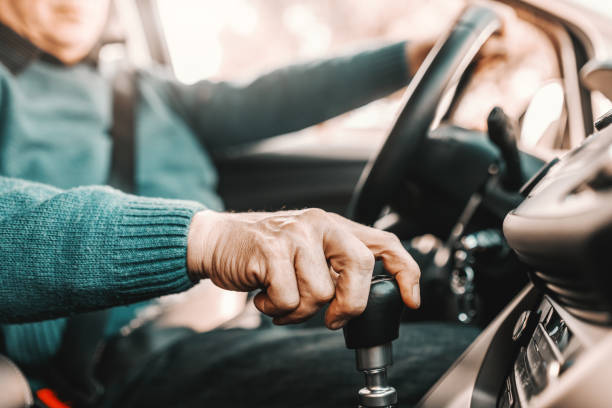 Close up of senior man holding one hand on gearshift and other on steering wheel while sitting in his car. Selective focus on hand. Close up of senior man holding one hand on gearshift and other on steering wheel while sitting in his car. Selective focus on hand. gearshift photos stock pictures, royalty-free photos & images