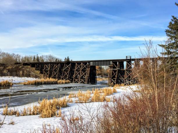 Walking along a pathway beside the Sturgeon River in St. Albert, Alberta, Canada.  The snow and ice are melting and there is an old wooden train bridge in the background. stock photo