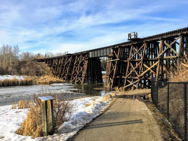Walking along a pathway beside the Sturgeon River in St. Albert, Alberta, Canada.  The snow and ice are melting and there is an old wooden train bridge in the background. stock photo