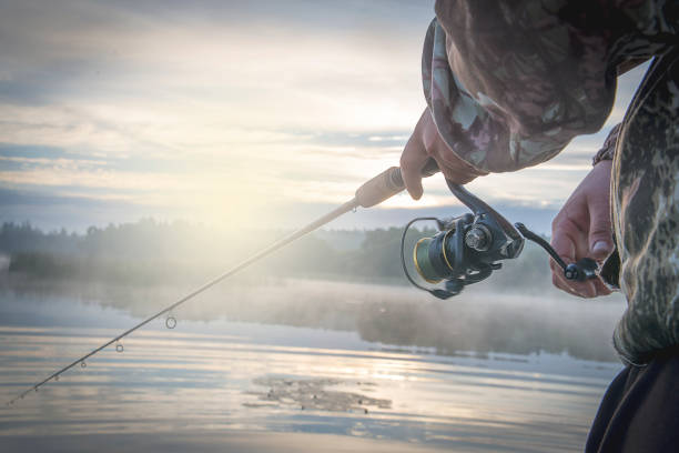 un hombre con un giro en el crepúsculo de la mañana en la orilla del río. - fishing reel fotografías e imágenes de stock