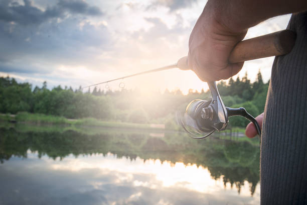 человек с спиннингом в утренние сумерки на берегу реки. - bass angling стоковые фото и изображения