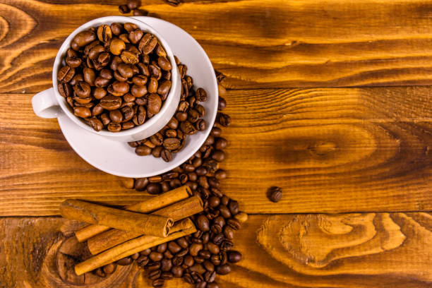istock White cup filled with coffee beans and cinnamon sticks on wooden table. Top view 1137875537