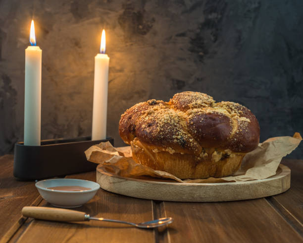 Sweet Challah bread on a wooded round plate on wooden brown table with honey and two candles on Shabbat evening making Kidush / black  background with copy space . close up stock photo