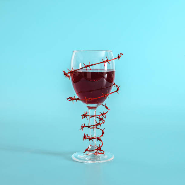 wine glass with red wine wrapped with barbed wire on blue background. the concept of danger of alcoholism, addiction, refusal of alcohol. minimal concept. - alcoholism narcotic excess alcohol imagens e fotografias de stock