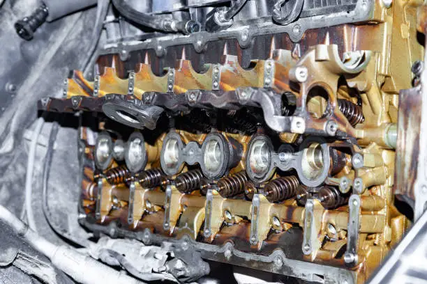 A six-cylinder in-line engine under the hood of the car with the valve cover removed with traces of yellow oil during repairs in a vehicle service workshop. Warranty repair in auto service.
