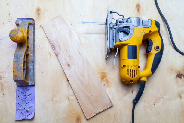 istock Flat lay of a yellow electric jigsaw and hand plane ready for work use on the workbench with sawn plywood in a workshop for carpentry work. Tool for industry and production. 1137891333