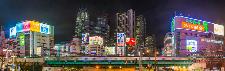 Commuter train zooming through the futuristic highrise cityscape and neon drenched night streets of Shinjuku in the heart of Tokyo, Japan’s vibrant capital city.