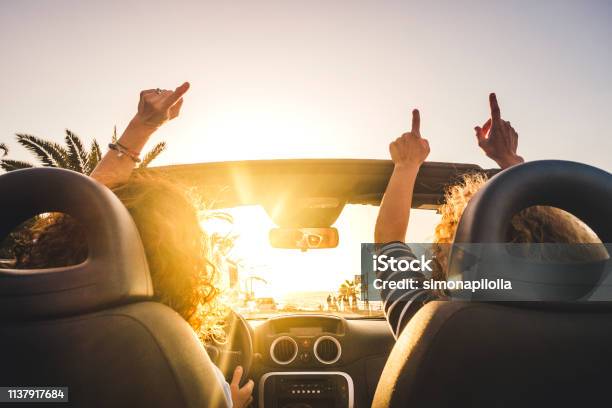 Couple Of Woman Friends Traveling And Driving Having A Lot Of Fun Dancing In The Car With Opened Roof And Summer Vacation Sunset Ocean In Front Concept Of Friendship Together And Nice Lifestyle For Independent Girls Stock Photo - Download Image Now