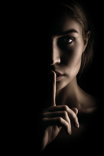 La chica muestra un signo de silencio. Cara sobre fondo negro, Close-up photo