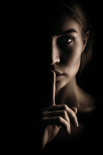 the girl shows a sign of silence. face on black background, close-up - finger on lips imagens e fotografias de stock