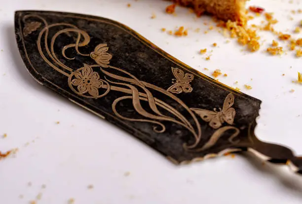 One beautifully decorated cake server with engraved flowers and butterflies on a white plate, next to cake crumbs - close-up, horizontal landscape orientation