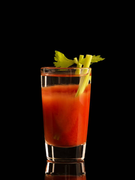bloody mary cocktail in glasses with straws and lime on wooden board near salt, pepper, tomatoes and celery
