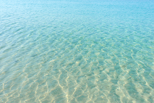 Clear blue water ripple on sandy beach. Sea water reflections surface. Tropical sunny summer day.