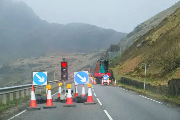 Red light at road works and traffic cones with safety sign at rural isolated mountain scene uk