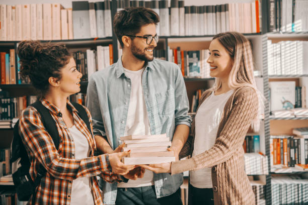 istock Three cheerful students standing in library and holding books they need for school project. In background shelves with books. 1137926950