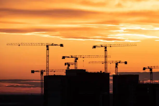 Photo of Crane and building silhouettes at sunrise. Abstract Industrial background with construction cranes silhouettes over amazing sunset sky