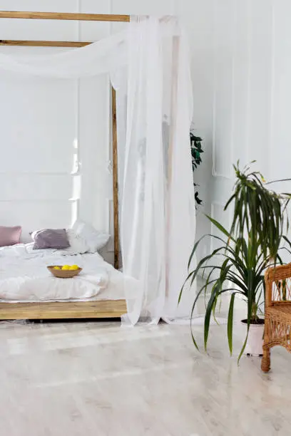 Beautiful bright room and a four-poster bed. Cozy bedroom in light colors with a wooden floor, a large four-poster bed and basket of flowers. Scandinavian simplicity design. Eco loft apartments.