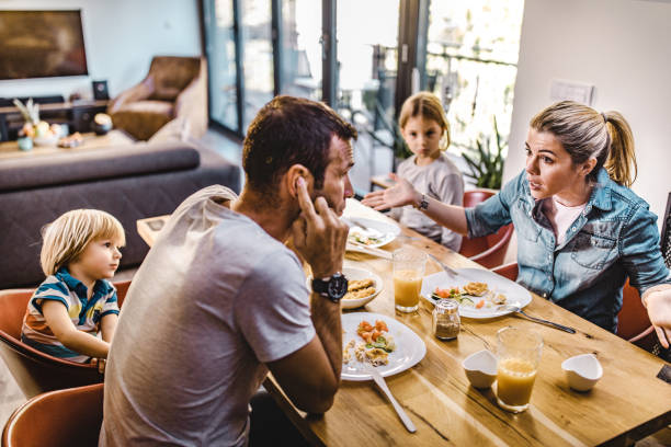 los padres jóvenes discuten mientras almorzan con sus hijos en casa. - discusión fotografías e imágenes de stock