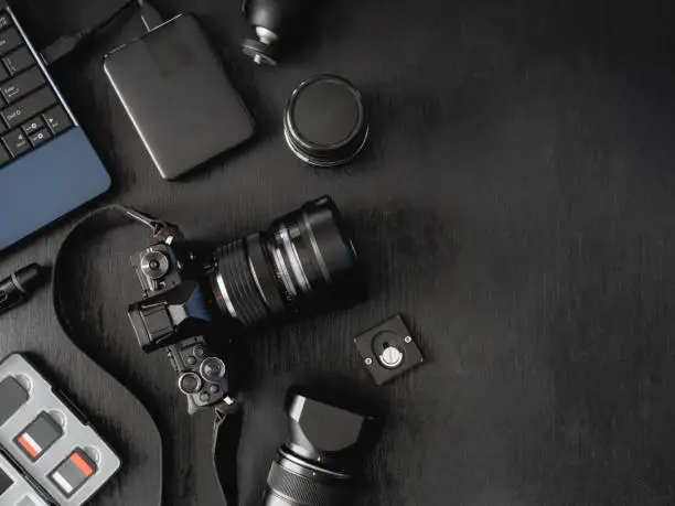 Photo of top view of work space photographer with digital camera, flash, cleaning kit, memory card, external harddisk, USB card reader, laptop and camera accessory on black table background