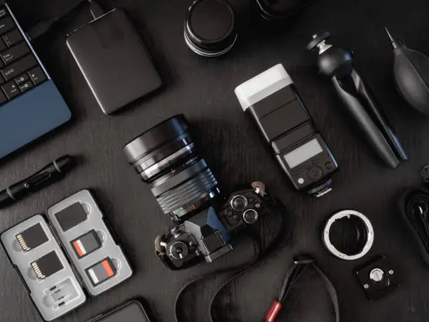 top view of work space photographer with digital camera, flash, cleaning kit, memory card, external harddisk, USB card reader, laptop and camera accessory on black table background