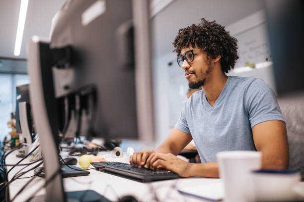 joven programador afroamericano trabajando en pc de sobremesa en la oficina. - profesional de informática fotografías e imágenes de stock