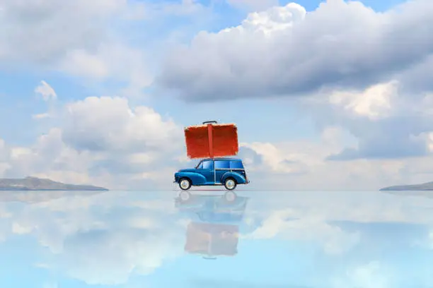 Photo of Old car with a suitcase on the trunk with reflection against the blue sky with beautiful clouds. Copy space travel concept.