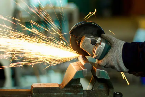 Man working with hand tools. hands and sparks close-up. production of parts. Angular grinding machine cuts metal with sparks.