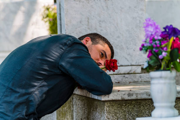 emotional gestresst mann in schwarzem kneeling vor grab seines verstorbenen freundes - spooky cemetery single flower flower stock-fotos und bilder