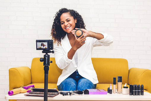 African american woman blogger in front of camera recording vlog herself talking about with makeup cosmetics for internet social networks at home