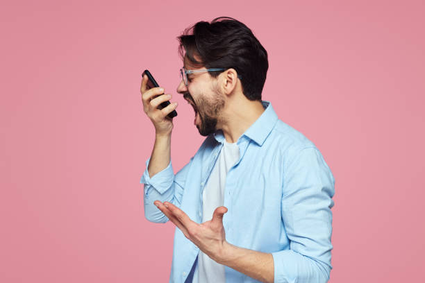 retrato de un joven empresario furioso gritando en el teléfono móvil aislado sobre fondo rosado. - furious blue little boys caucasian fotografías e imágenes de stock