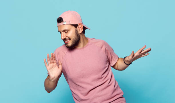 guapo chico alegre con ropa elegante y gorra de béisbol rosa bailando felizmente sobre fondo azul - child lifestyles isolated blue fotografías e imágenes de stock