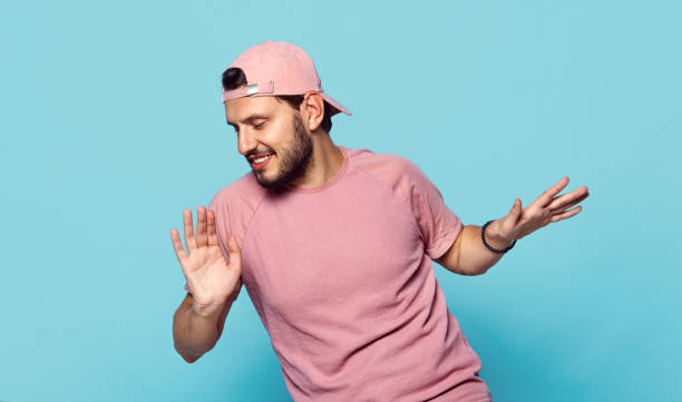 bel ragazzo allegro con abiti eleganti e berretto da baseball rosa che balla felicemente su sfondo blu - pink hat foto e immagini stock