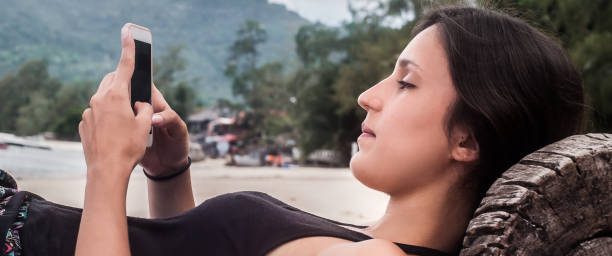 istock Young woman with smartphone relaxing on tropical beach 1137966379