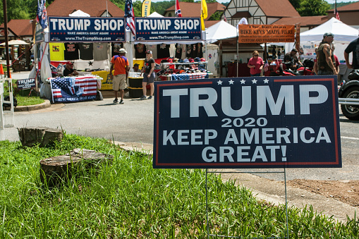 Helen, GA, USA - June 2, 2018:  A Donald Trump 2020 presidential election campaign sign sits in the grass in front of the Trump Shop, a popup outdoor store selling Trump apparel and other items in a parking lot on June 2, 2018 in Helen, GA.