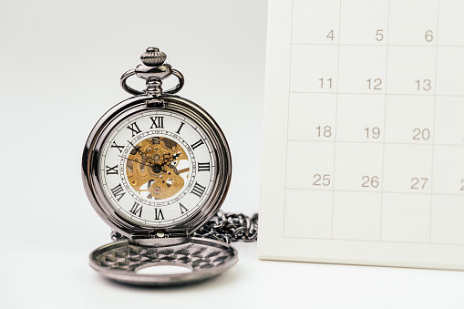 Vintage pocket watch with white clean desktop calendar on white background using as time passing, time management, year change or deadline concept.