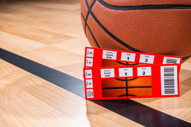 A pair of basketball tickets sitting next to a ball with arena wood floor in the background stock photo