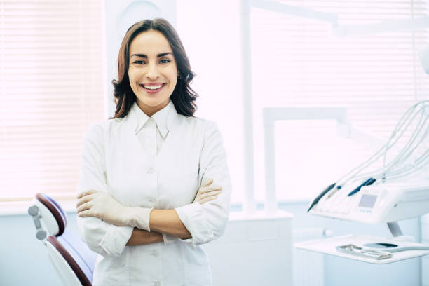 pronti a lavorare! una ragazza con un abito bianco e guanti medici con gli occhi luminosi nocciola e il sorriso sincero sul viso nell'armadietto del dentista è pronta a dare un trattamento ai suoi pazienti. - nurse paramedic healthcare and medicine hygiene foto e immagini stock